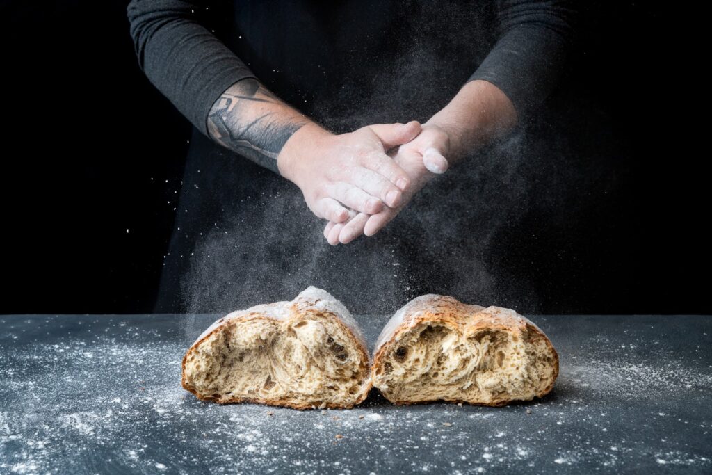 Fotografia kulinarna pieczywa: piekarz rozsypuje mąkę nad świeżym chlebem, profesjonalna sesja zdjęciowa pieczywa