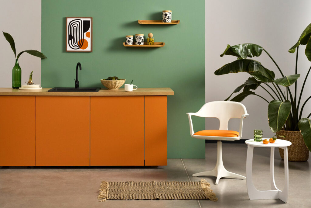 Sesja aranżacyjna kuchnia: nowoczesna kuchnia z zieloną ścianą, pomarańczowymi szafkami i dekoracjami roślinnymi